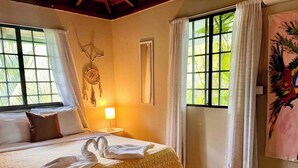 A hotel room with a bed, a dreamcatcher, a window with curtains, and a painting on the wall. - Mi Zaru Sea View Animal Paradise (Quepos)