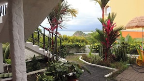 A garden with tropical plants, a thatched roof structure, and a view of the sea. - Mi Zaru Sea View Animal Paradise (Quepos)