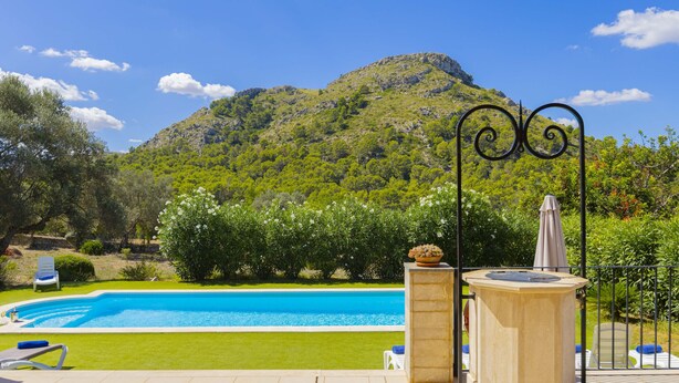A swimming pool with a view of a mountain, surrounded by greenery and a tiled patio area. - Villa Es Garrover (Alcúdia)