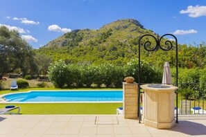 A swimming pool with a view of a mountain, surrounded by greenery and a tiled patio area.