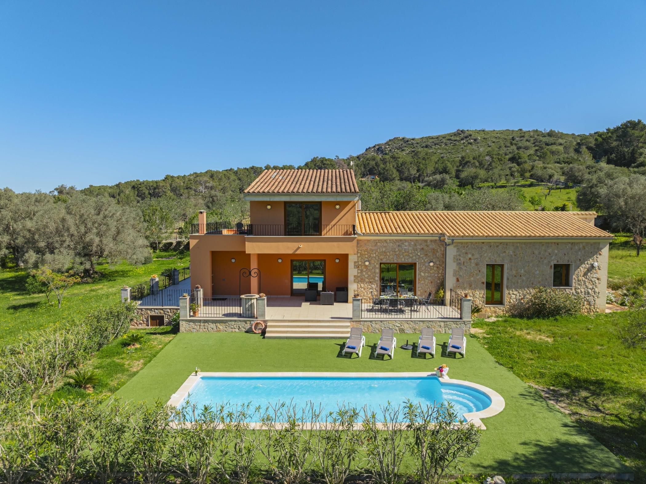 A two-story house with a swimming pool, outdoor furniture, and a stone wall.