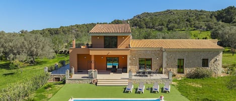 A two-story house with a swimming pool, outdoor furniture, and a stone wall.