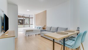 A modern living room with a sofa, a dining table, and a TV mounted on the wall. - Home2Book Modern Studio in Las Palmas, Only Adults (Las Palmas de Gran Canaria)