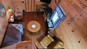 Interior acogedor de una cabaña con una mesa redonda central, paredes de madera y un espacio de estar cómodo.