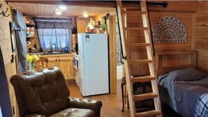 Una cabaña pequeña con kitchenette, una escalera de madera, una cama y un sillón de cuero marrón.