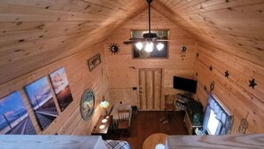 Interior de una cabaña de madera con comedor, ventilador de techo y televisor montado en la pared.