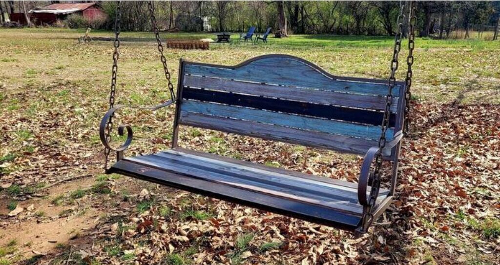 Un banco de madera con cadenas de metal, rodeado de hojas secas y un campo cubierto de hierba.