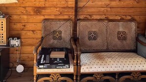 Un interior de madera con un televisor de pantalla plana montado en la pared, un banco de madera con cojines tejidos, y una pequeña mesa con una regleta y una bolsa.