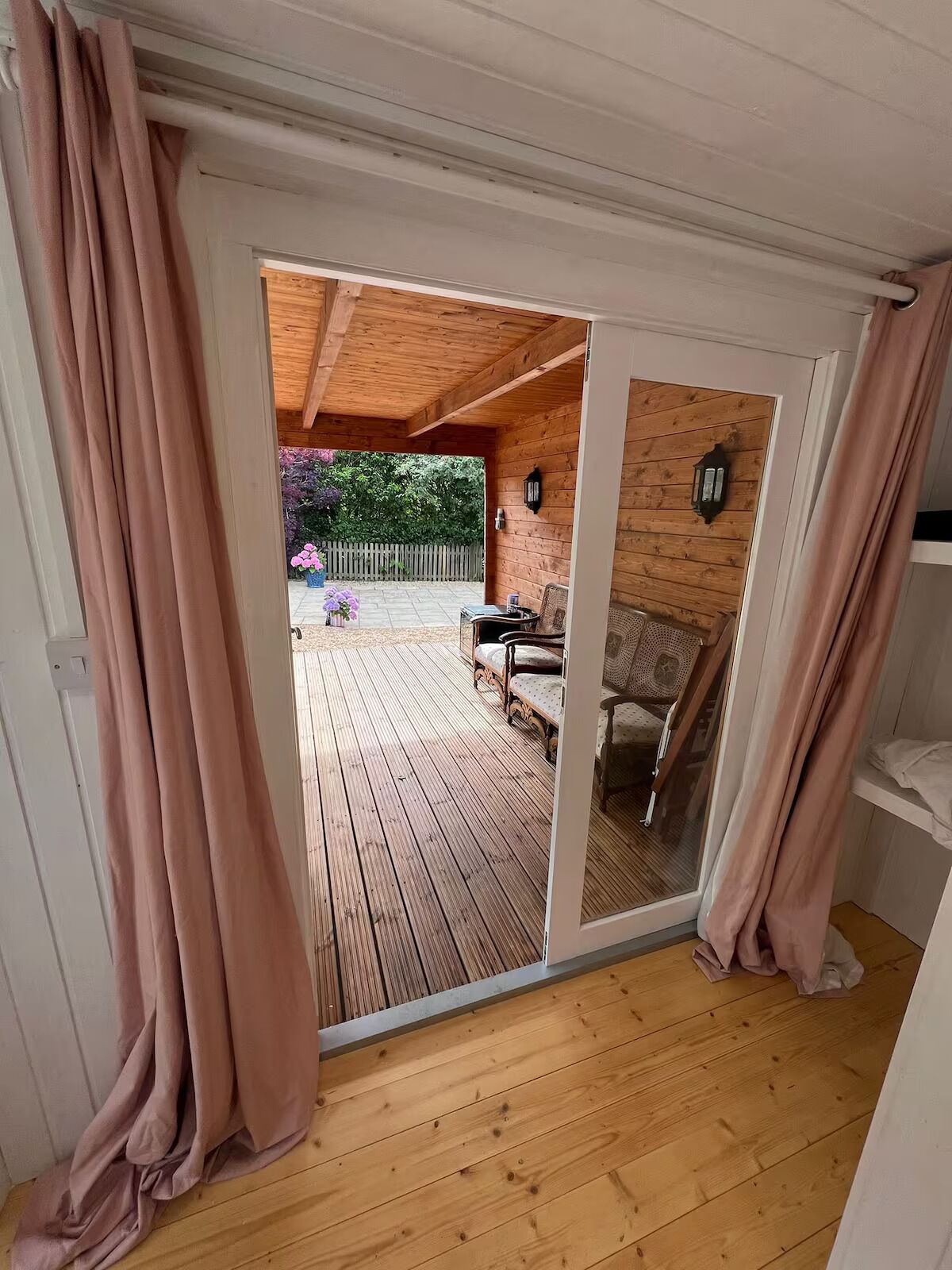 Un terrazza in legno con una porta scorrevole in vetro che si apre su un patio esterno con tavolo e sedie.