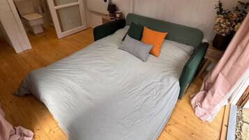 A bedroom with a bed, wooden flooring, a nightstand, a lamp, and a window with curtains.