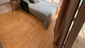 Un dormitorio con cama, piso de madera, paredes blancas, tragaluz y vistas al exterior.