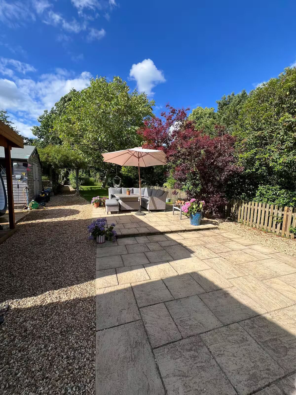 Een terras met stenen vloer, tuinmeubels en een pergola.