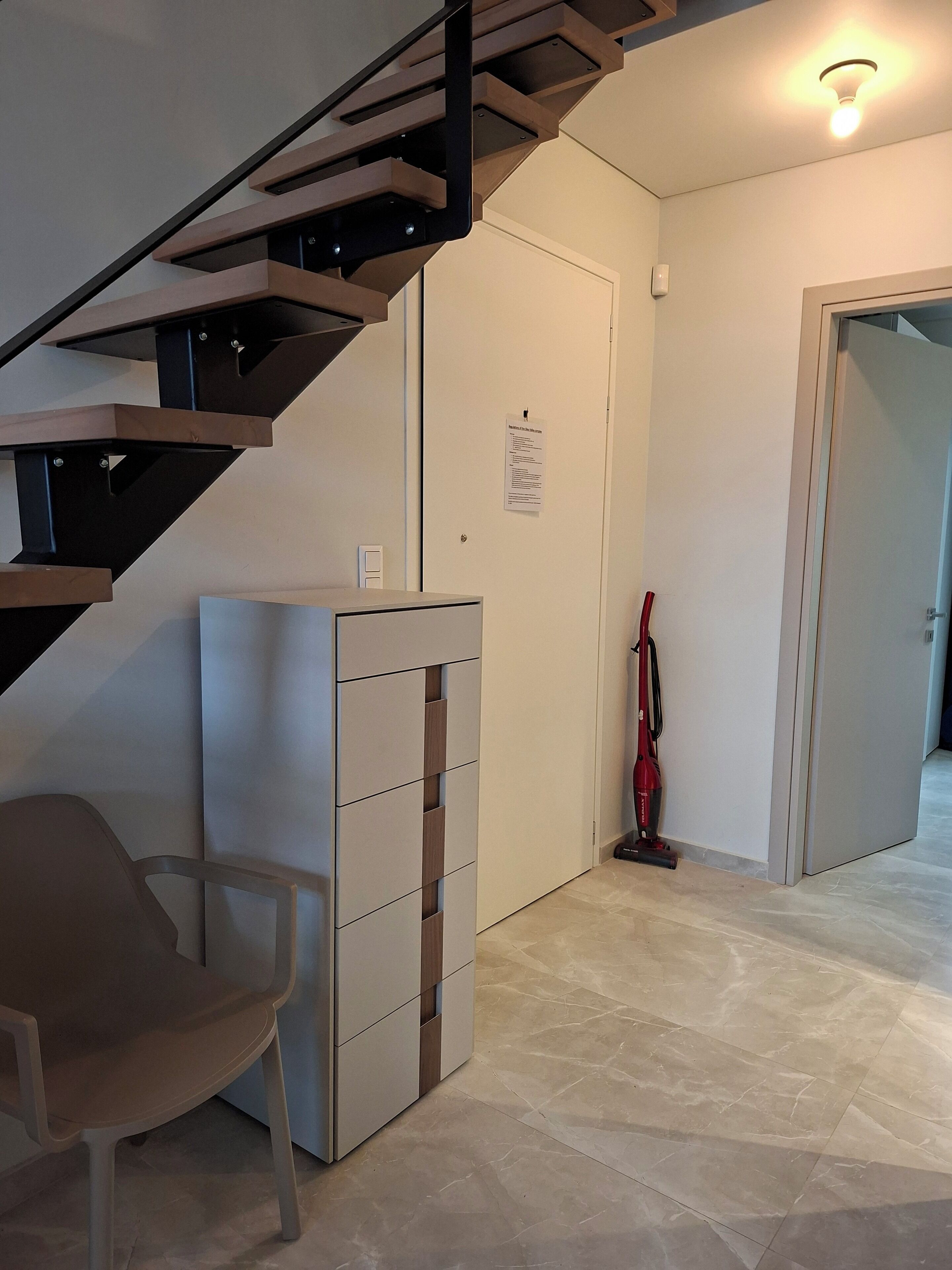 Un interior modern amb una escala, un moble d'emmagatzematge, un aspirador i una cadira.