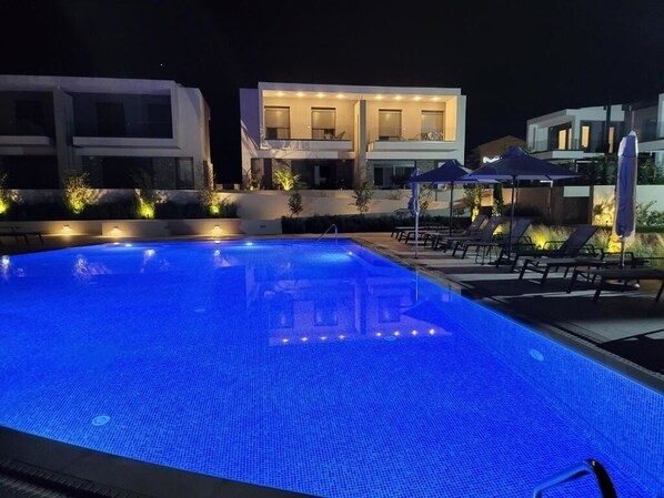 Une piscine à l’eau bleutée, entourée de bâtiments modernes et de chaises longues.