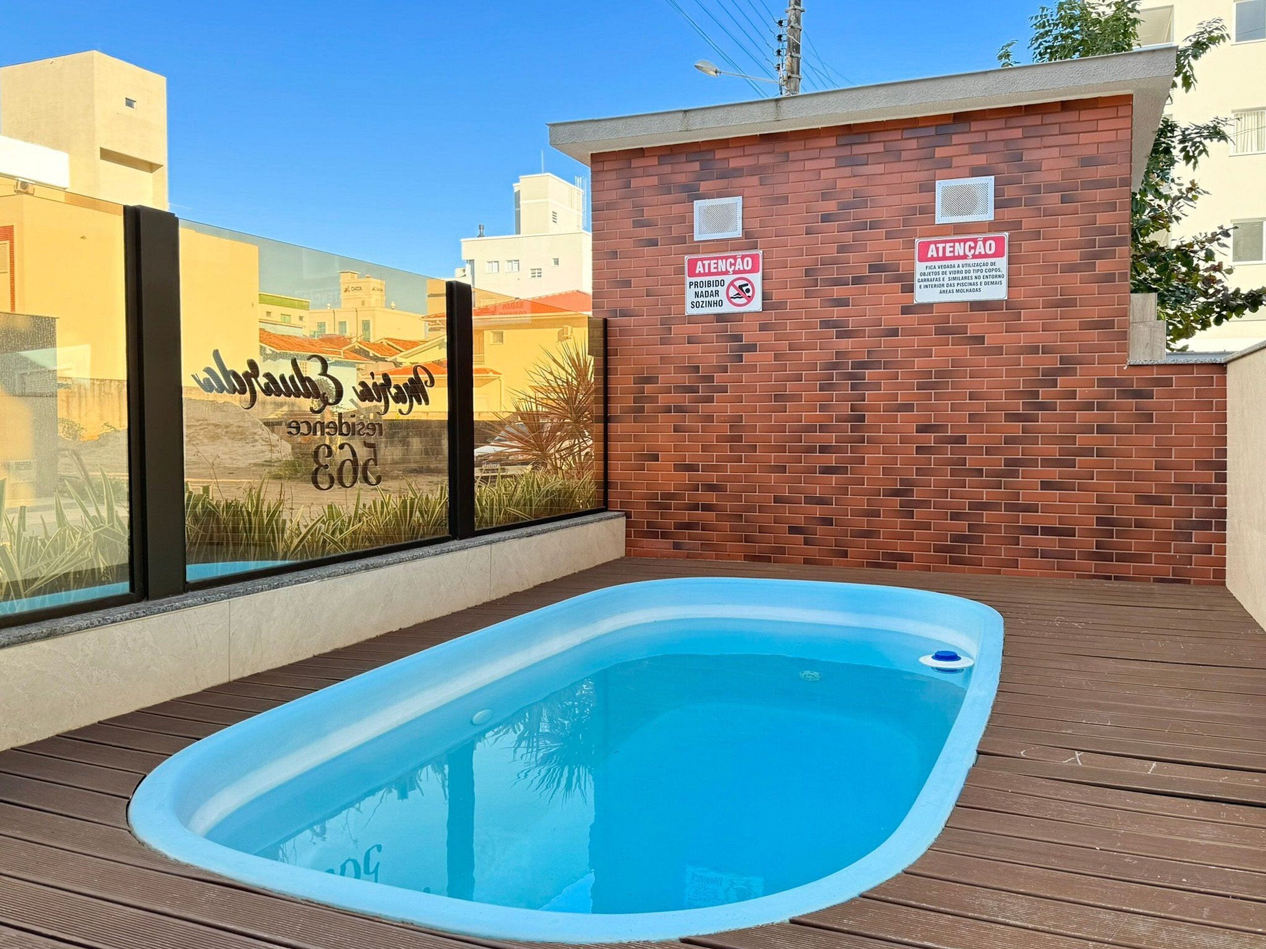 A swimming pool with a wooden deck, a brick wall, and two signs.