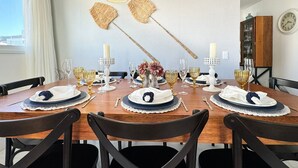 A dining area with a wooden table set for four, featuring white and gold tableware, candles, and a decorative fan. - Brisa de Palmas - Res. Maria Eduarda (Governador Celso Ramos)