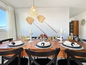 A dining area with a wooden table set for four, featuring white and gold tableware, candles, and a decorative fan. - Brisa de Palmas - Res. Maria Eduarda (Governador Celso Ramos)