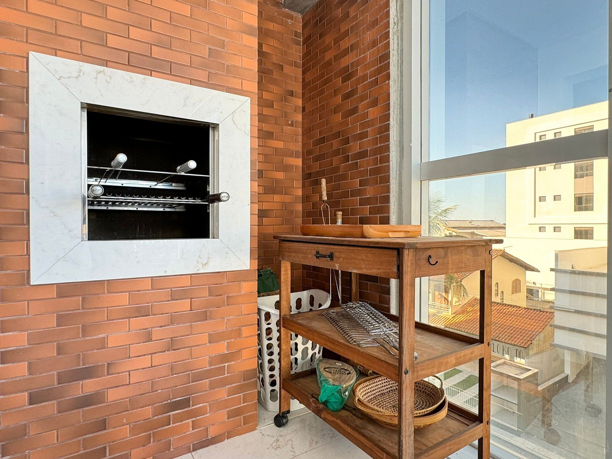 Un balcón con pared de ladrillo, una parrilla, una mesa de madera y vista a edificios.