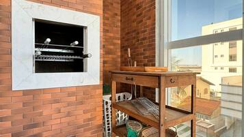 Un balcón con pared de ladrillo, una parrilla, una mesa de madera y vista a edificios.