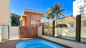 A swimming pool with a wooden deck, a brick wall, and a sign in Portuguese. - Brisa de Palmas - Res. Maria Eduarda (Governador Celso Ramos)