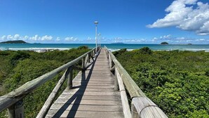 A wooden boardwalk leading to a beach with a clear view of the ocean and distant islands. - Brisa de Palmas - Res. Maria Eduarda (Governador Celso Ramos)