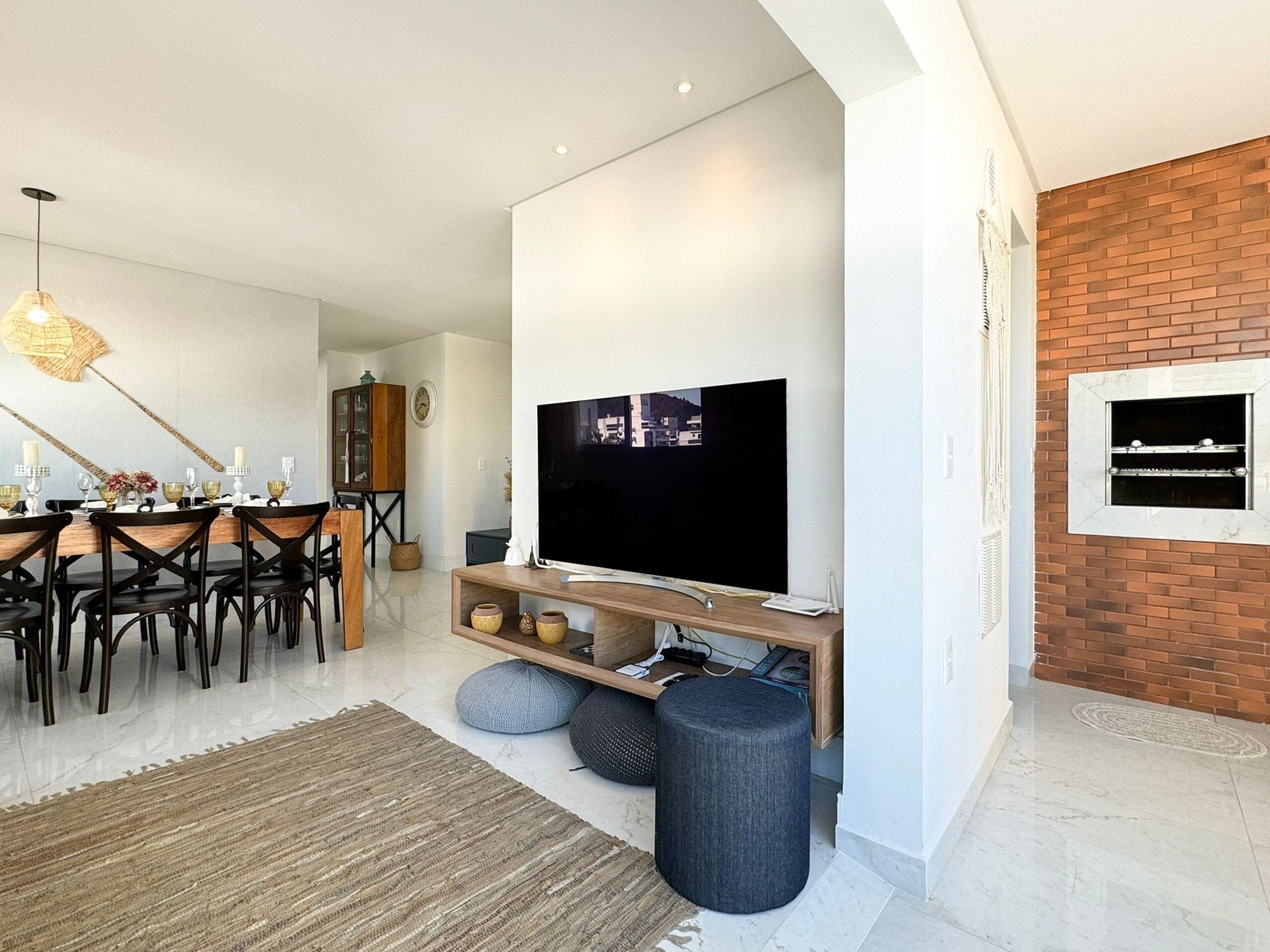 Ein modernes Wohnzimmer mit einem Flachbildfernseher auf einem Holzboden, einem Essbereich mit einem Holztisch und Stühlen sowie einer Wand mit Ziegelverkleidung.