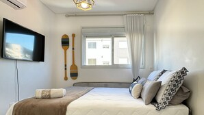 A bedroom with a bed, a TV, a window with curtains, and a wall-mounted air conditioner. - Brisa de Palmas - Res. Maria Eduarda (Governador Celso Ramos)