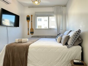 A bedroom with a bed, a TV, a window with curtains, and a wall-mounted air conditioner. - Brisa de Palmas - Res. Maria Eduarda (Governador Celso Ramos)