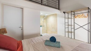 A bedroom with a bed, a wardrobe with hanging clothes, and a bathroom with a shower.