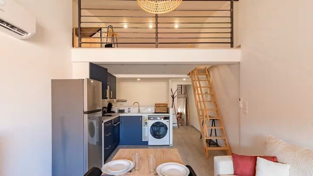 A compact kitchen with modern appliances, a dining area with a wooden table and chairs, and a staircase leading to an upper level.
