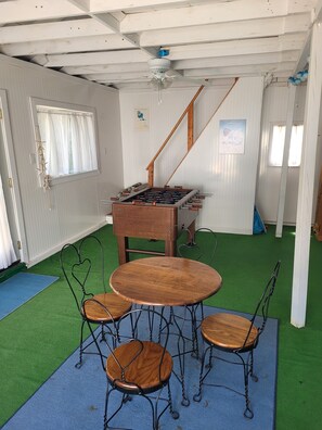 A room with a foosball table, a wooden table with chairs, and a green carpet.