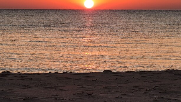 A sunset over a calm sea with a beach in the foreground. - "Huron Winds" a charming 3-bedroom house just steps from Lake Huron in Oscoda (Oscoda)