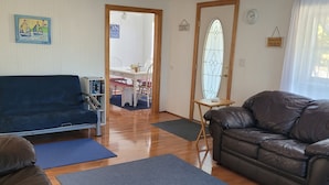 A living room with a blue sofa, a brown leather sofa, and a dining area with a white table and chairs. - "Huron Winds" a charming 3-bedroom house just steps from Lake Huron in Oscoda (Oscoda)