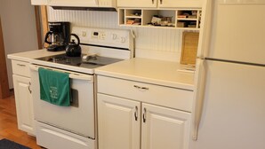 A kitchen with white cabinetry, a stove, a microwave, and a refrigerator. - "Huron Winds" a charming 3-bedroom house just steps from Lake Huron in Oscoda (Oscoda)