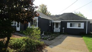 A two-story house with a dark exterior, a front porch, and a visible mailbox. - "Huron Winds" a charming 3-bedroom house just steps from Lake Huron in Oscoda (Oscoda)