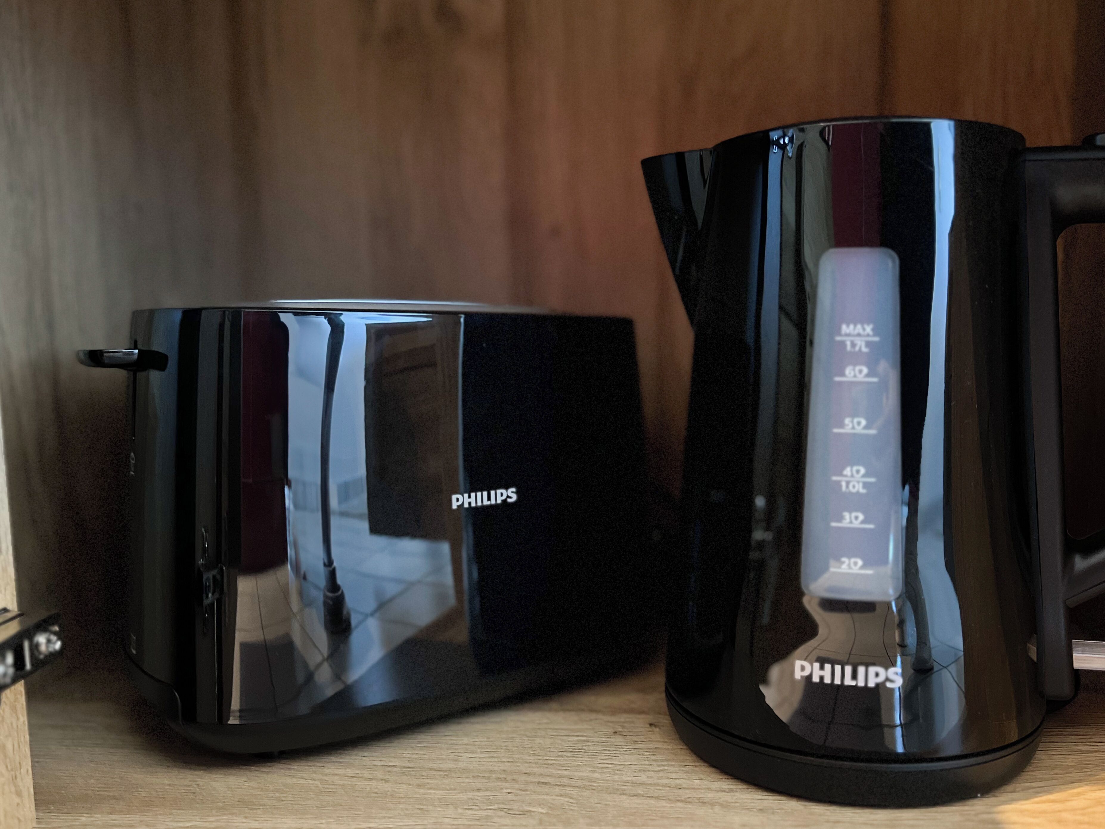 A black Philips coffee maker and a black Philips electric kettle on a wooden surface.