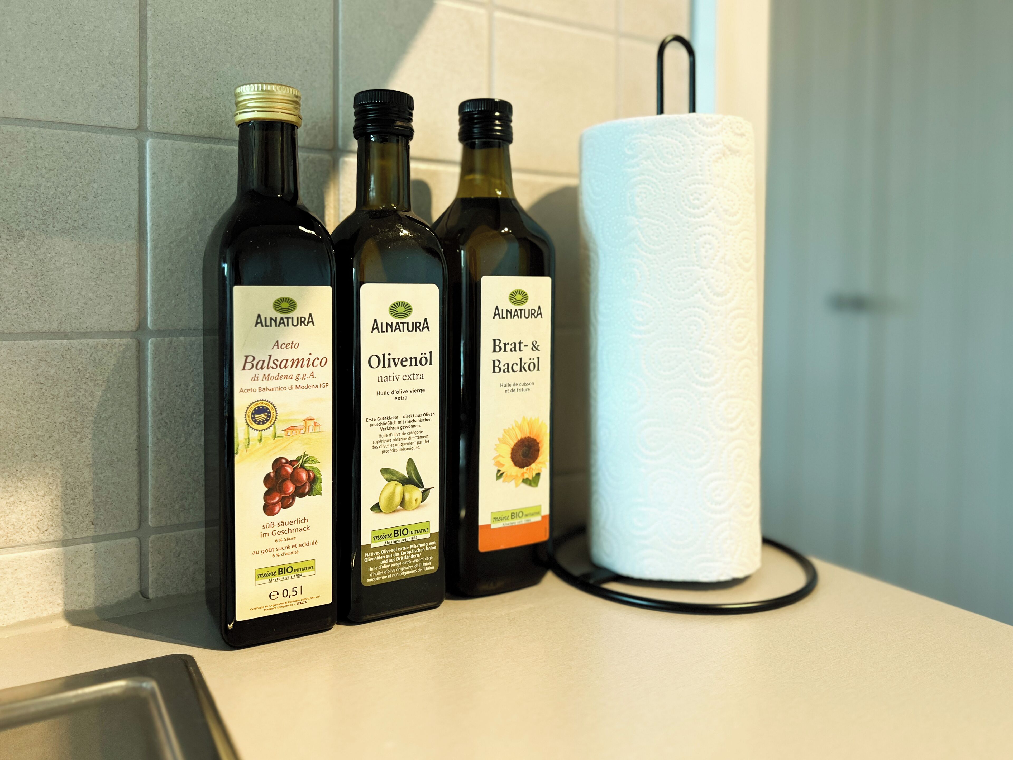 Three bottles of Alnatura olive oil on a kitchen counter next to a roll of paper towels.