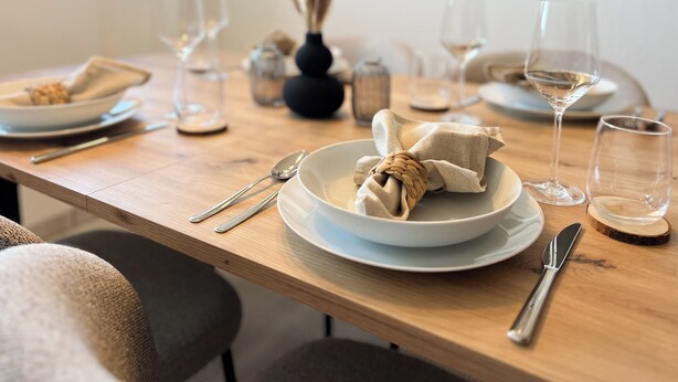 Een eettafel gedekt met borden, bestek en glazen.