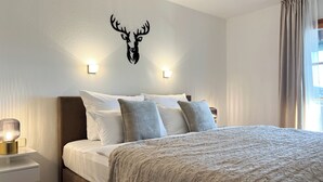 Hotelkamer met een bed, een op de muur bevestigd decoratie van een hertenkop, twee wandlampen en een raam met gordijnen.