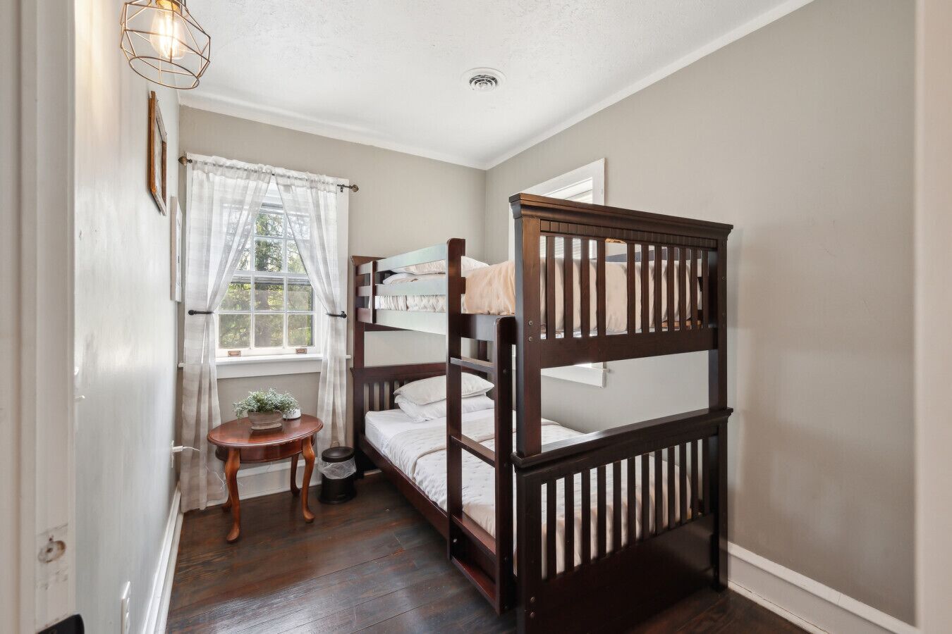 A small, cozy room with a bunk bed, a small round table, and a window with sheer curtains.