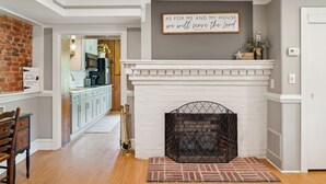 Une cuisine moderne avec des armoires blanches, un mur d’accent en briques et une cheminée surmontée d’une enseigne décorative.