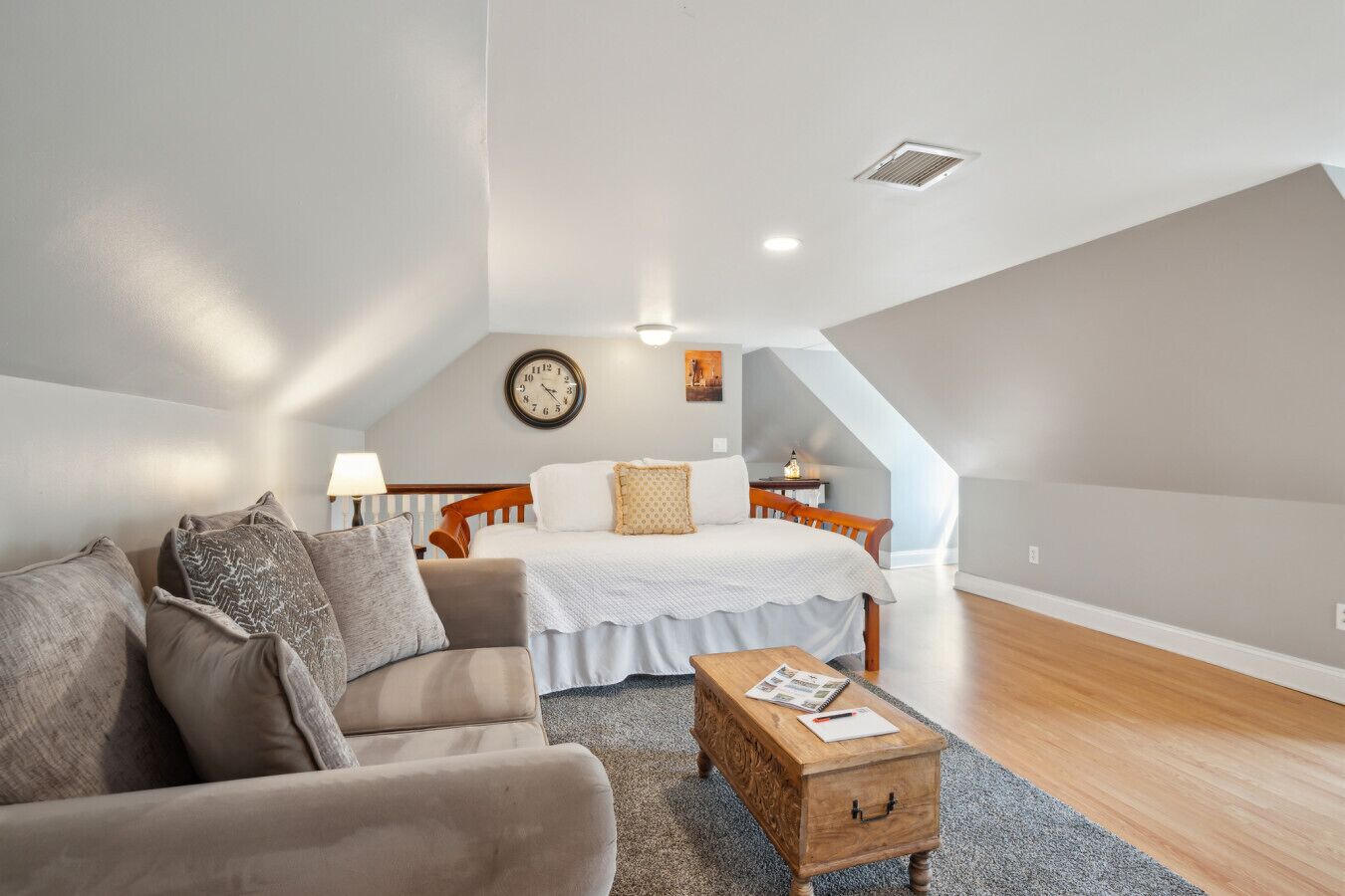 Ein gemütliches Schlafzimmer im Loft-Stil mit Bett, Sofa, einer hölzernen Kommode und einem kleinen Tisch.