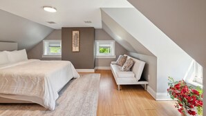Una camera da letto con un letto, una poltrona, due finestre, una lampada a soffitto e un quadro appeso al muro.