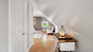 Un corridoio stretto con soffitto inclinato, una porta bianca a sinistra e un piccolo tavolo con una candela accesa a destra.
