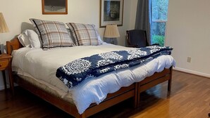 Un dormitorio con cama de madera, ventilador de techo, ventana con vista a árboles y un espejo en la pared.