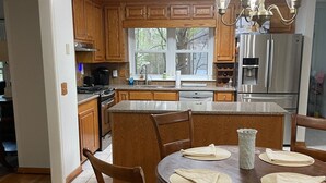 Una cocina moderna con armarios de madera, un refrigerador de acero inoxidable, una mesa de comedor con sillas y una araña.