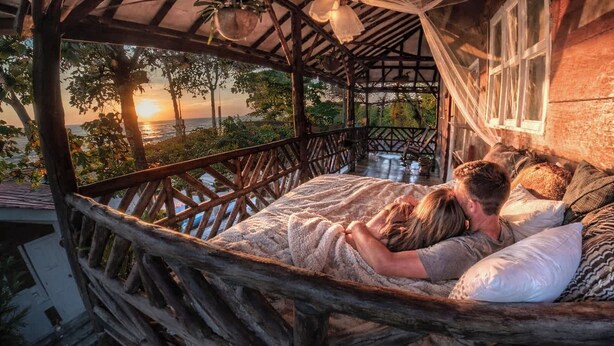 A couple lying in a rustic wooden hammock bed with a view of the sunset over the ocean. - Oceanfront King Room with Private Balcony, Pool & A/C (Pochomil)