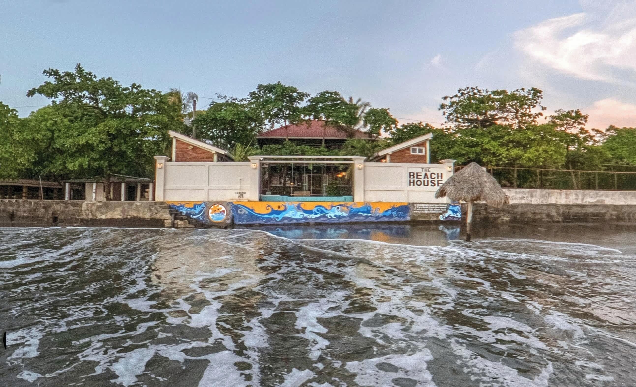 Une maison de plage avec un toit de chaume et une piscine au premier plan.