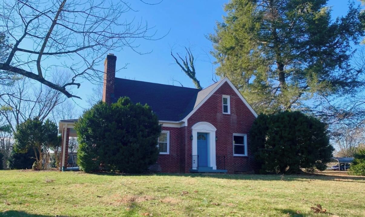 A two-story brick house with a gabled roof, a front porch, and a chimney.