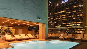Una piscina interior con sillones de descanso y vistas a un rascacielos de noche.